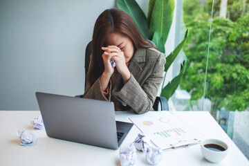 Businesswoman get stressed with screwed up papers and laptop on table while having a problem at...