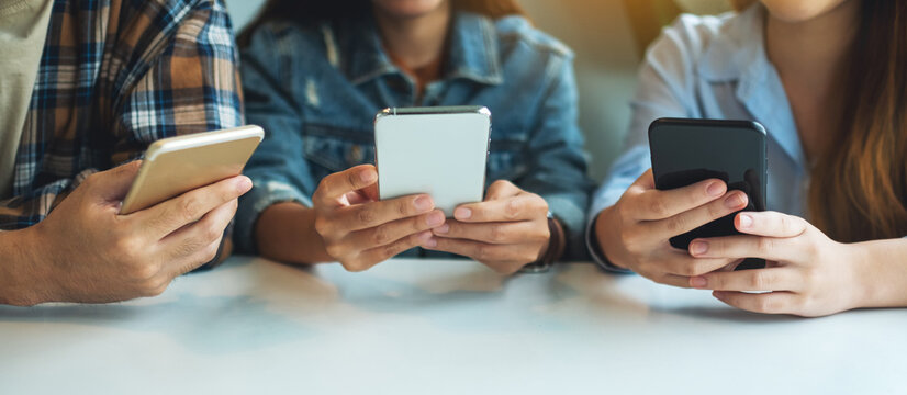 Group of young people using and looking at mobile phone while sitting together