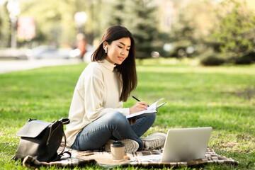 Girl writing in diary, sitting in parkland near university