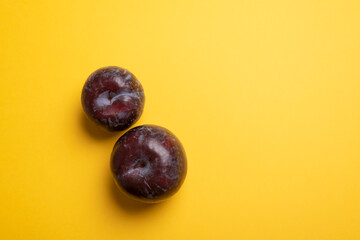 Purple plum flat lay over yellow desk. Two blue plums and big yellow copy space area. Ready for adding text