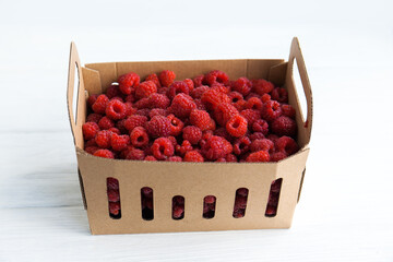 Fresh raspberries in a box on a white table