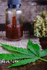 brown medical cannabis resin extract in bottle of medicine dropper. next to marijuana buds and hemp leaf. on hemp sack. Wooden backdround on rust metal suface. vertical