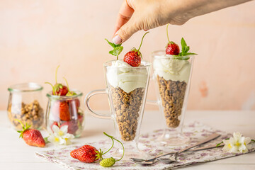 Woman hand decorated healthy breakfast with granola and greek yogurt fresh raw strawberry.