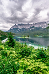 Fototapeta na wymiar Small islands with pine-trees in the middle of Eibsee lake with Zugspitze mountain. Beautiful landscape scenery with paradise beach and clear blue water in German Alps, Bavaria, Germany, Europe.