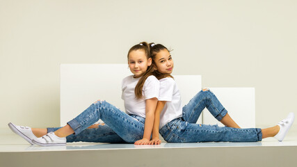 Two little girls posing in the studio on white cubes