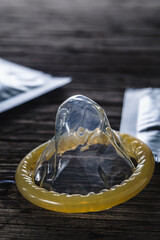 world sexual helth day. the unpacked condom lies next to the packed cones on an old wooden background. dramatic frame. copy space. vertical.