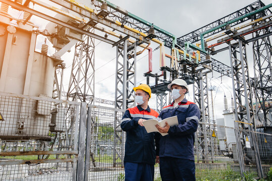 Engineers electrical substations conduct a survey of modern high-voltage equipment in the mask at the time of pandemia in the evening. Energy. Industry