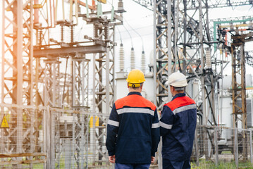 Two specialist electrical substation engineers inspect modern high-voltage equipment during sunset....