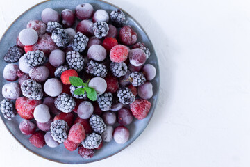Frozen berries in a gray plate with a sprig of mlisa on a white background. Copy space. Top view. Close-up