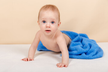 Laughing baby wearing diaper and blue towel on bed after bath, shower