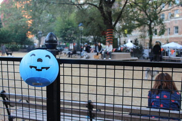 A blue Halloween pumpkin bucket hanging on a fence - Dog Park in New York City, United States.