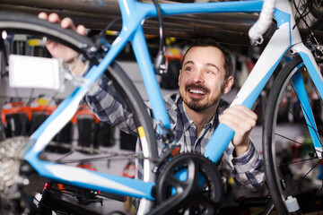 Smiling american man checks bicycle frame in shop when choosing bike.