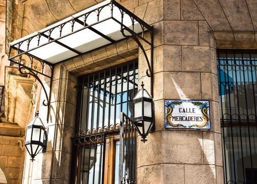 Picture of a corner in Mercaderes Street, Havana. A building with a stone wall and a decorated sign with the name of the street.