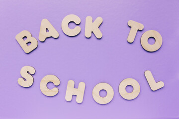 Inscription BACK TO SCHOOL made from wooden letters on purple background. The concept of the...