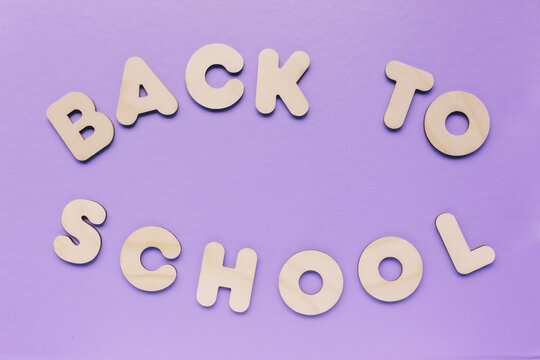 Inscription BACK TO SCHOOL made from wooden letters on purple background. The concept of the importance of education.