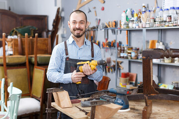 Cheerful craftsman with carpentry tools posing in furniture restoration studio