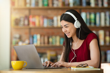 Smiling asian girl in headphones looking at laptop screen, studying at cafe