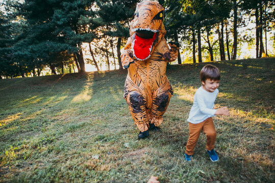 Person Wearing Dinosaur Costume Chasing Boy In Park