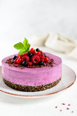 Homemade raw cashew blackcurrant cake on chocolate granola, garnished with fresh berries on a plate. Sugar, lactose, gluten free.