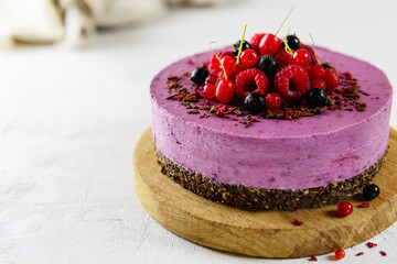 Raw cashew blackcurrant cake on chocolate granola, garnished with fresh berries. Sugar, lactose, gluten free. Horizontal orientation, copy space.