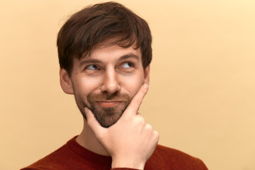 Need to choose. Photo of young man with beard wearing sweater, holds chin, purses lips with...