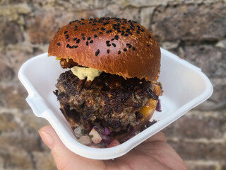 Gourmet street food burger served in a styrofoam container and isolated against a brick background 