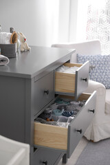 Modern open chest of drawers with clothes and accessories in baby room