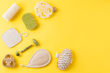 Tools for beauty routine from ecological material. Zero waste bathroom. Jade face roller, anti cellulite massager, loofah and bamboo sponges on yellow. Copy space, flat lay
