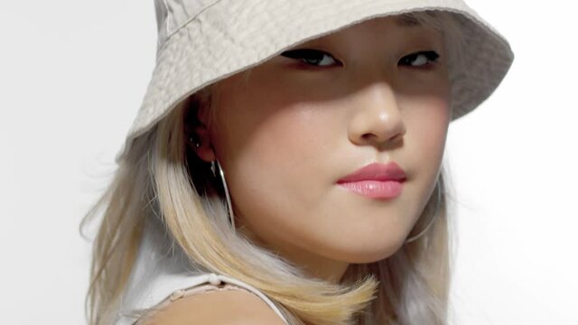 tilted up portrait of blonde korean model with fresh natural makeup wearing a bucket hat and watching to the camera