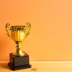 Champion golden trophy on wooden table with orange background