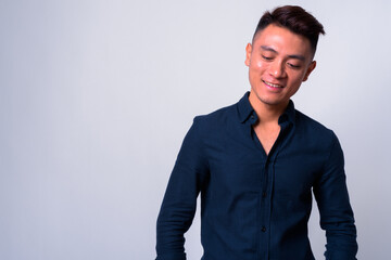 Portrait of happy young Asian businessman thinking and looking down