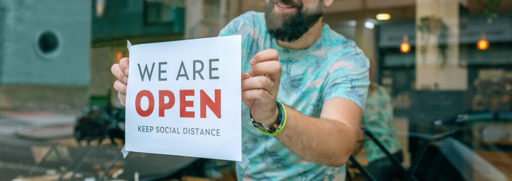 Happy man placing opening poster after coronavirus on the glass of his business