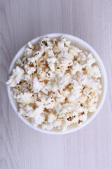 Salted popcorn in a bowl on a wooden table. Top view