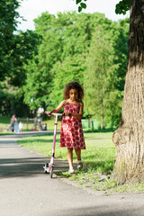 Little black girl with a kick scooter in a city park