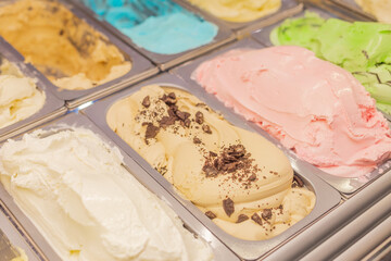 Multi-colored ice cream of natural delicate pastel colors: beige chocolate, green pistachio taste, vanilla, pink, strawberry, blue, cream in metal trays in the refrigerator in candy store