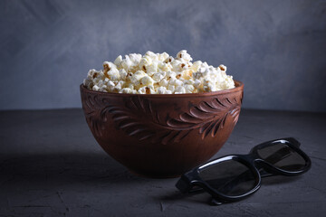 Salted popcorn in a bowl with 3D glasses on a table on a gray background. Front view