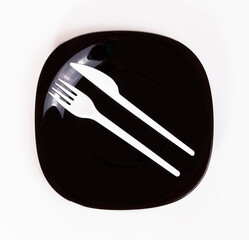 White knife and fork on black plate isolated on white background