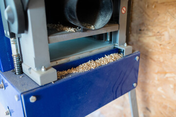 Wood chips in focus on blue industrial wood jointing planing machine.