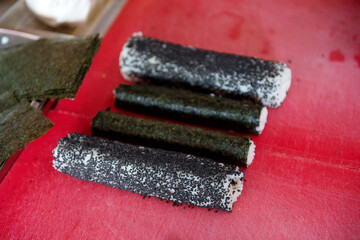 Several blanks for sushi before cutting into pieces on a red kitchen board, close-up.