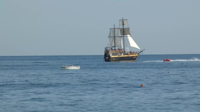 Stylized pirate ship in the sea. Sailing vessel moving in the water,  lot of boats and hydrocycles around. Summer entertaiments. Sunny day, Black Sea near Sochi.