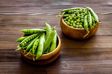 Set of green pea pods in wooden bowl on kitchen table desk
