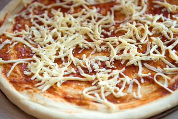 Pizza dough piece with grated cheese and tomato sauce, close-up.