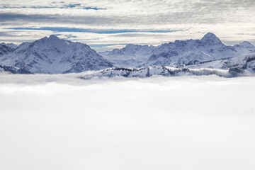 Snow covered mountains with inversion valley fog and trees shrouded in mist. Scenic snowy winter landscape in Alps, Allgau, Kleinwalsertal, Bavaria, Germany.