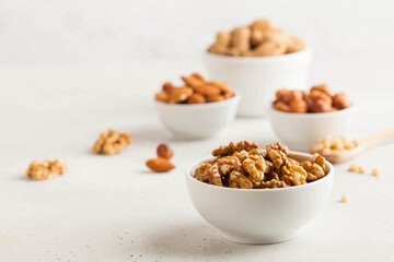 A handful of walnuts in a white bowl, assorted nuts on a light background. Healthy snacks, healthy...