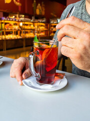 Close-up of a transparent cup with fruit tea. A man holds a teaspoon in his hands. A cafe.