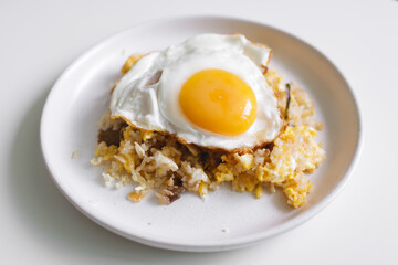 Homemade fried rice with fried egg on top served on white dish.
