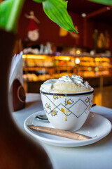 Close-up of a white cup with cappuccino on the table. Cafe interior, flowers in a vase.
