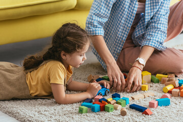 cropped view of nanny and kid playing with multicolored blocks of floor