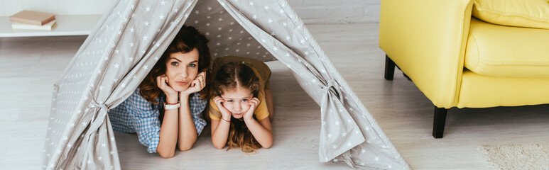 horizontal image of nanny and kid looking at camera while lying in toy wigwam © LIGHTFIELD STUDIOS