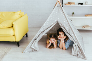 high angle view of beautiful nanny and cute child looking at camera while lying in toy wigwam © LIGHTFIELD STUDIOS